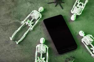 esqueletos decorativos ficam perto do smartphone em um fundo escuro. foto