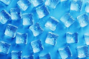 muitos cubos de gelo gelados e refrescantes com gotas em um background azul foto