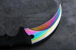 um punhal com uma lâmina de aço com uma cor gradiente em um fundo preto. foto