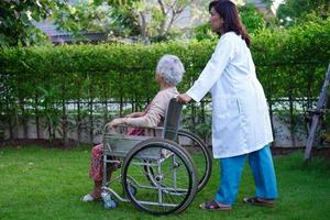 médico ajuda paciente idosa asiática com deficiência sentada na cadeira de rodas no parque, conceito médico. foto