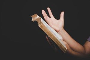 close-up da mão da mulher cristã segurando a bíblia sagrada orar e adorar para agradecer a Deus na igreja com fundo preto, pessoa adulta do sexo feminino está lendo livro, foto