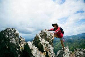 jovem caminhadas feminina escalada no topo da rocha, mulher mochila olhando o vale da bela montanha à luz do sol no verão, paisagem com garota esporte, colinas altas, floresta, céu. viagem e Turismo. foto