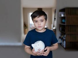 menino feliz segurando o cofrinho com rosto sorridente. retrato de uma criança alegre mostrando caixa de economia de dinheiro criança da escola aprendendo responsabilidade financeira e planejando economizar para o futuro conceito foto