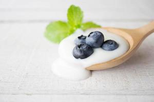 iogurte branco com folha de hortelã e mirtilo fresco na colher de pau no fundo branco de madeira. foco seletivo. foto