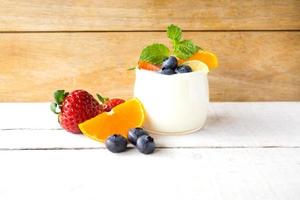 iogurte branco natural em vidro com frutas frescas na mesa de madeira branca. foto