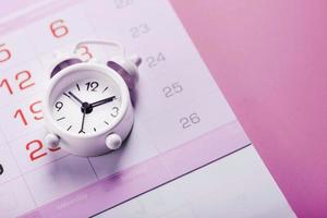 calendário com um despertador branco em um fundo rosa. foto