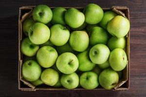 maçãs verdes maduras e suculentas em uma caixa em uma mesa de madeira. foto