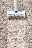 um aspirador de pó sem fio limpa o tapete na sala de estar com a parte inferior das pernas com uma faixa limpa foto
