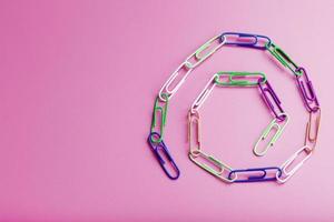 uma cadeia de clipes de papel multicoloridos em um fundo rosa foto
