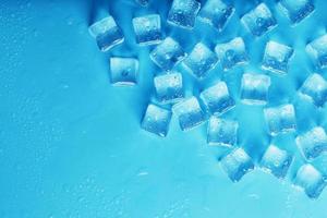 cubos de gelo com gotas de água espalhadas sobre um fundo azul, vista superior foto