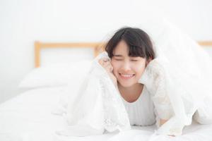 belo retrato jovem mulher asiática mentindo e sorria enquanto acorda com o nascer do sol de manhã, menina com feliz e divertido no quarto, estilo de vida e conceito de relaxamento. foto