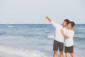 retrato homossexual jovem casal asiático em pé apontando algo juntos na praia no verão, ásia gay indo mar para lazer com romântico e feliz em férias no mar, lgbt com conceito legal. foto