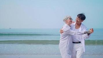 casal de aposentados asiáticos relaxantes à beira-mar no verão. uma mulher sênior dançando com seu parceiro na praia. foto