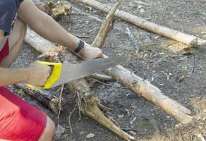 um homem corta um tronco de árvore para lenha com uma serra manual. foto