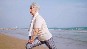 mulher idosa asiática se exercitando na praia. mulher aposentada, alongamento antes de correr. foto