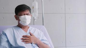 velho asiático está hospitalizado com covid-19. paciente do sexo masculino idoso usando uma máscara médica senta-se na cama do paciente. foto