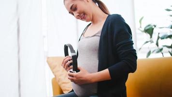feliz mulher grávida asiática colocando fones de ouvido na barriga dela. foto