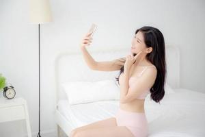 bela jovem asiática sexy em cueca falando uma selfie em smartphone para rede social no quarto, garota de lingerie relaxe tirando uma foto no celular na cama no quarto.