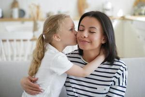 garotinha filha adotiva beijo mãe abraço em casa. maternidade feliz, adoção de criança foto