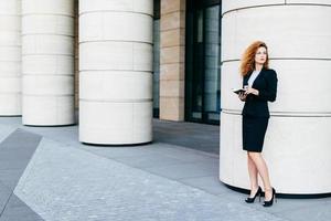 retrato horizontal de empresária bonita vestida com roupas formais e sapatos pretos com salto alto, segurando o livro de bolso, olhando de lado com expressão pensativa. conceito de carreira e negócios foto