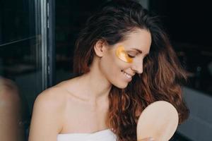 jovem mulher feliz fazendo cabelo diário e cuidados com o rosto. mulher penteia o cabelo e aplica tapa-olhos. foto