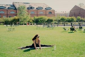 foto de jovem modelo feminino ativo se divide no karemat focado na distância vestida com roupas esportivas permanece flexível motivado para poses de treinamento ao ar livre leva um estilo de vida saudável. esporte em nossa vida