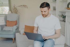 jovem sério usando computador portátil para trabalho remoto em casa foto