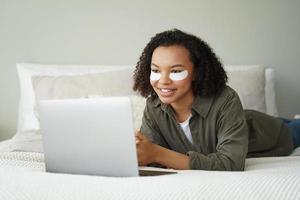 garota birracial com tapa-olhos no rosto trabalha no laptop. rotina de cuidados faciais matinais, beleza foto