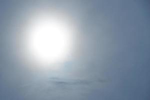 um grande disco solar brilha através das nuvens. fundo azul e branco. foto com espaço de cópia.