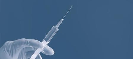 mão de luva branca do médico segurando uma seringa com líquido transparente isolado sobre fundo azul. vacina antiviral. foto