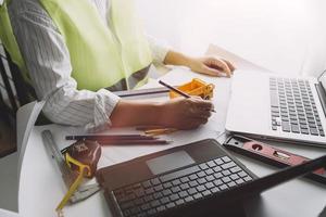 dois colegas discutindo dados de trabalho e tablet, laptop com projeto arquitetônico no canteiro de obras na mesa no escritório foto