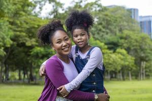 mãe afro-americana está abraçando sua filha enquanto faz um piquenique de verão no parque público para o conceito de amor e felicidade foto