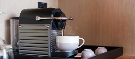 mão fazendo café expresso por máquina de café com cápsulas na mesa de madeira foto