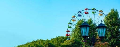 paisagem de um parque de diversões com lanterna decorada com flores de fundo a parte superior de uma roda gigante mostrando acima das copas das árvores contra um céu azul. foto
