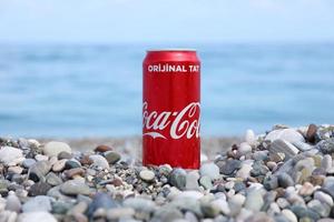 original coca cola red tin can encontra-se em pequenas pedras redondas perto da beira-mar. coca-cola na praia turca foto