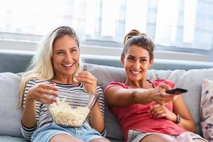 retrato de mulheres jovens engraçadas e felizes assistindo comédia na cama e rindo. amigos alegres comendo pipoca saborosa e olhando filme com alegria. ambiente acolhedor e amigável foto