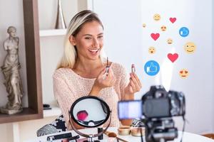 famoso blogueiro. alegre vlogger feminina está mostrando produtos cosméticos enquanto grava vídeo e dá conselhos para seu blog de beleza. foco na câmera digital foto