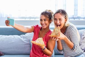amigos comendo pizza e sorrindo para selfie. eles estão compartilhando pizza e fazendo selfie no celular. eles estão fazendo festa em casa, comendo pizza e se divertindo. foto