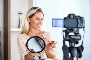 famoso blogueiro. alegre vlogger feminina está mostrando produtos cosméticos enquanto grava vídeo e dá conselhos para seu blog de beleza. foco na câmera digital foto