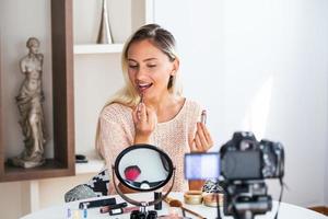 famoso blogueiro. alegre vlogger feminina está mostrando produtos cosméticos enquanto grava vídeo e dá conselhos para seu blog de beleza. foco na câmera digital foto