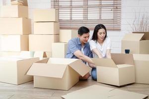 casal asiático se mudando para uma nova casa ajuda a desembalar a caixa de papel pardo para decorar a casa. conceito de começar uma nova vida, construir uma família. espaço de cópia foto