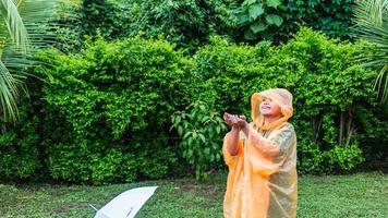 menino asiático vestindo capa de chuva laranja está feliz e se divertindo na chuva em um dia chuvoso. foto