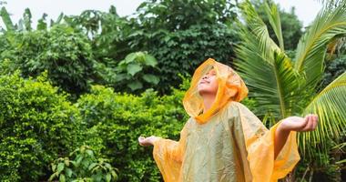menino asiático vestindo capa de chuva laranja está feliz e se divertindo na chuva em um dia chuvoso. foto