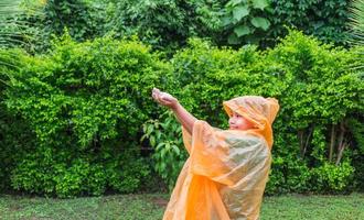 menino asiático vestindo capa de chuva laranja está feliz e se divertindo na chuva em um dia chuvoso. foto