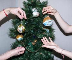 uma mão feminina decora a árvore de natal com brinquedos de natal e ano novo. a mão da mulher decora a árvore de natal com guirlandas. foto