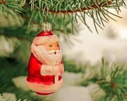 brinquedo de natal papai noel pendura em um galho coberto de neve de uma árvore de natal em um fundo festivo de neve branca bokeh com espaço de cópia. foto