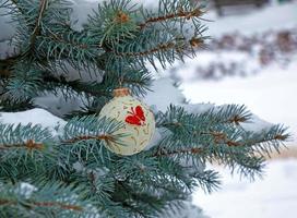 bola de natal pendurada em um galho coberto de neve de uma árvore de natal em um fundo festivo de neve branca e bokeh nevado com espaço de cópia foto