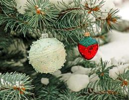 decorações de natal bola branca e morangos penduram em um galho coberto de neve de uma árvore de natal em um fundo festivo de neve branca bokeh foto