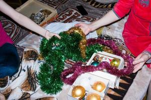 duas mulheres estão escolhendo decorações de natal para a árvore da casa. as mãos da mulher estão segurando guirlandas e brinquedos de natal. foto