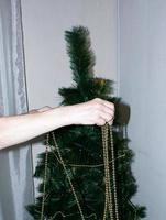 uma mão feminina decora a árvore de natal com brinquedos de natal e ano novo. a mão da mulher decora a árvore de natal com guirlandas. foto